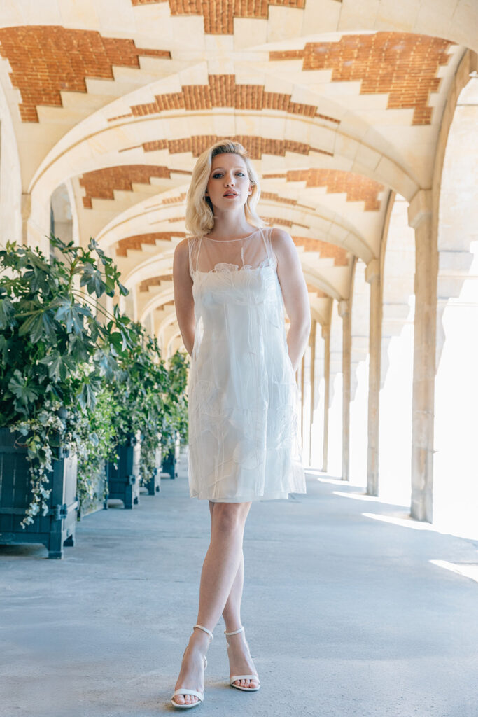 Femme dans la rue qui porte une robe de mariée court et un top en tulle brodé.