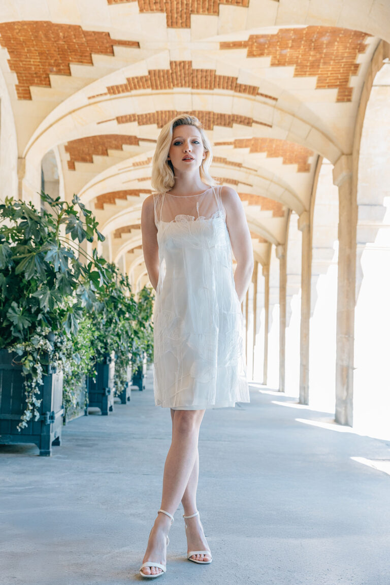 Femme dans la rue qui porte une robe de mariée court et un top en tulle brodé.
