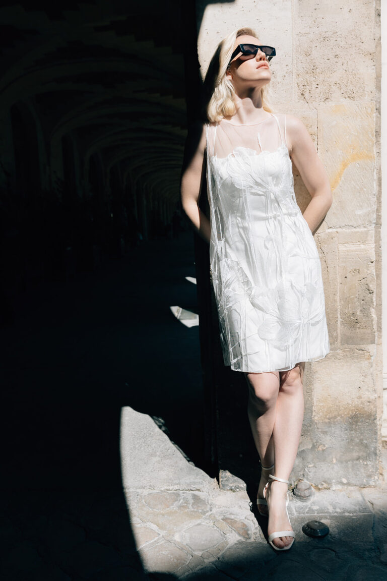 Femme dans la rue qui porte une robe de mariée court et un top en tulle brodé.