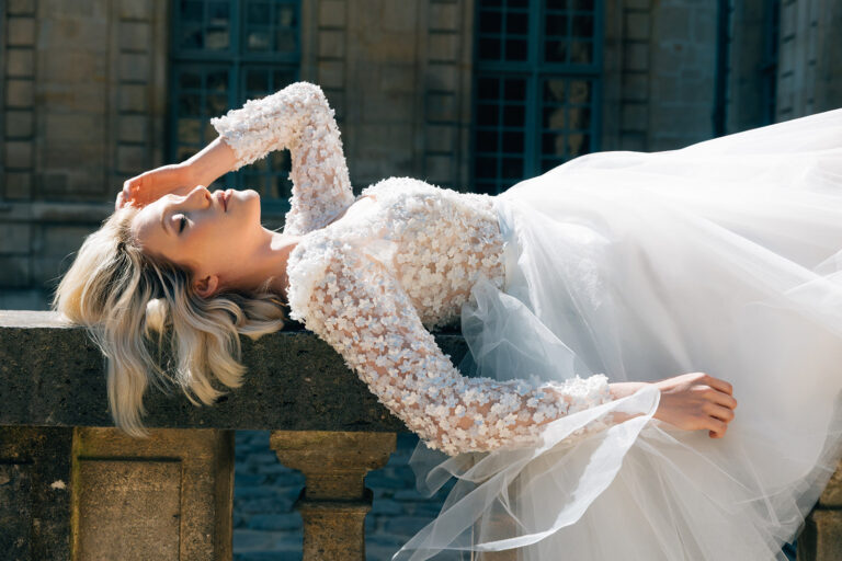 Femme allongée qui porte une robe de mariée courte en tulle à manches longues.