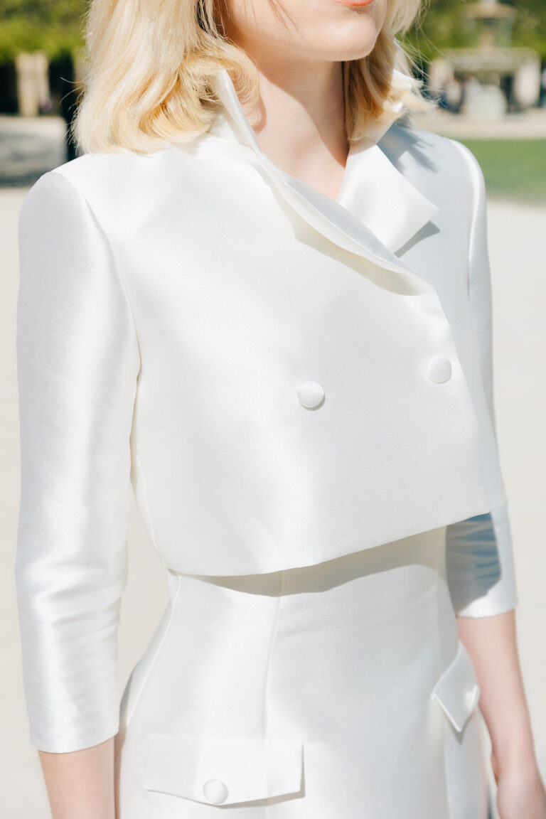 Veste de mariée blanche portée par une femme au dessus d'une robe de mariée en mikado.