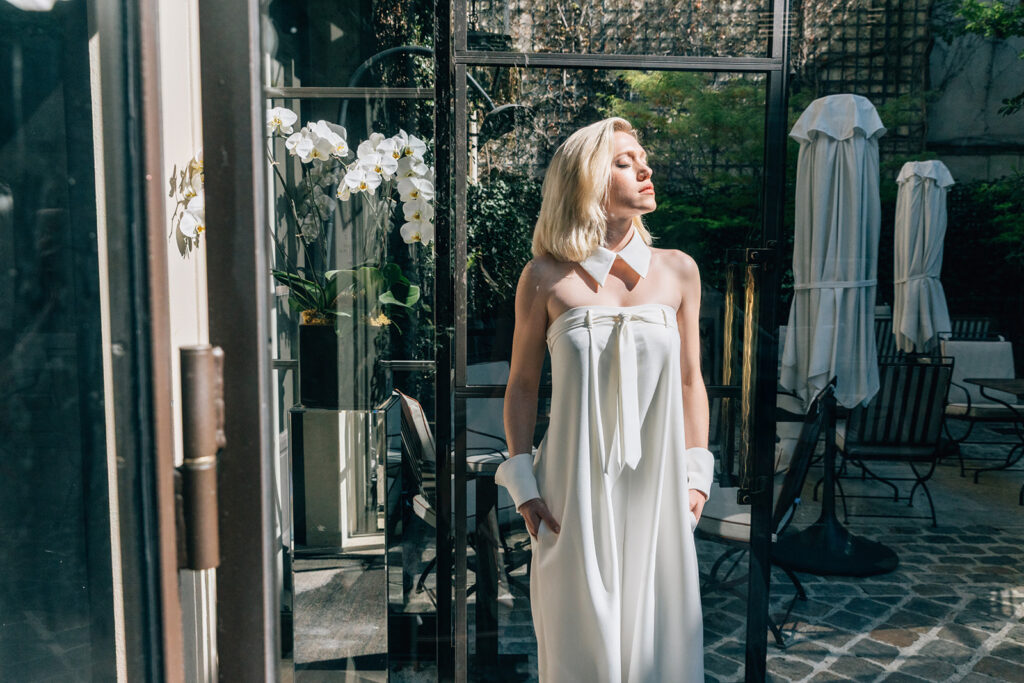 Femme qui a les mains dans les poches et qui porte une combinaison de mariée ample avec une cravate et les poignets et le col d'inspiration chemise.