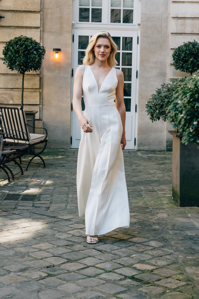 Femme qui marche et qui est vêtue d'une combinaison de mariée blanche et élégante.