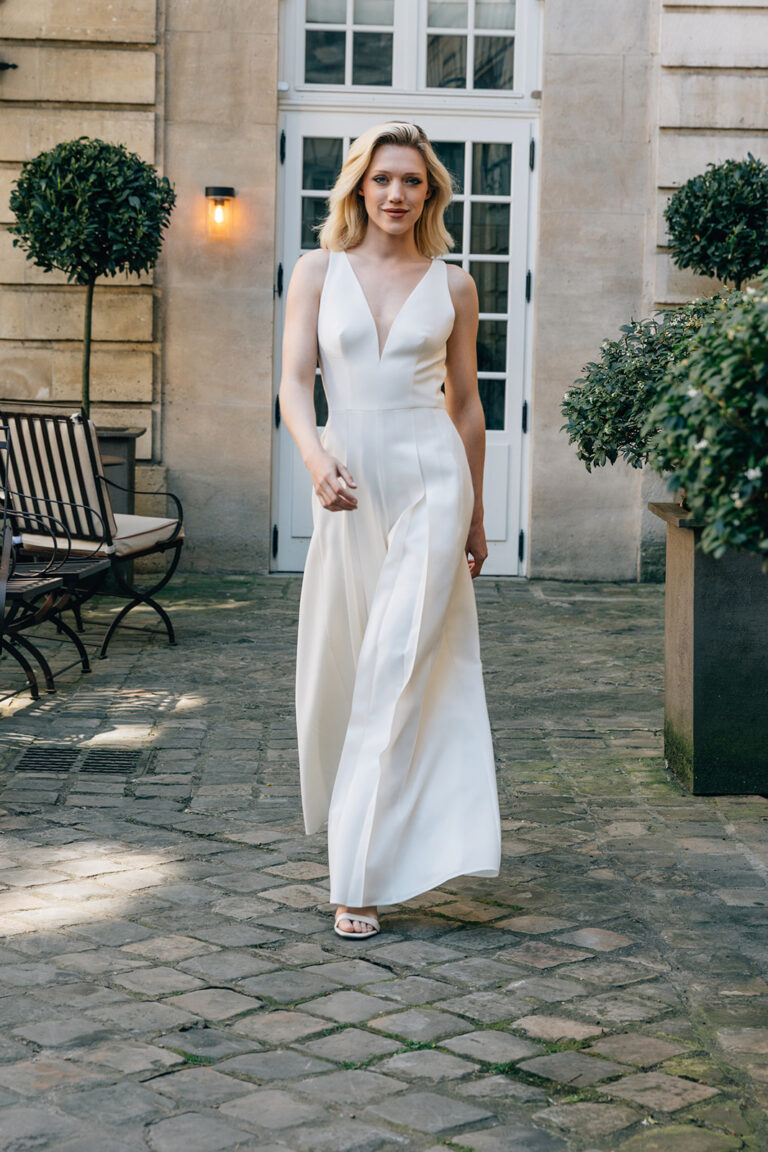 Femme qui marche et qui est vêtue d'une combinaison de mariée blanche et élégante.