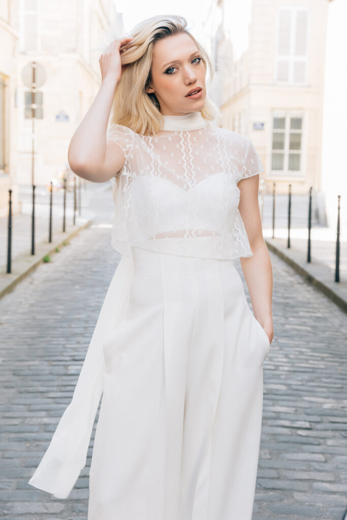 Femme portant une tenue de mariée blanche avec un pantalon et un top en dentelle de Calais-Caudry.