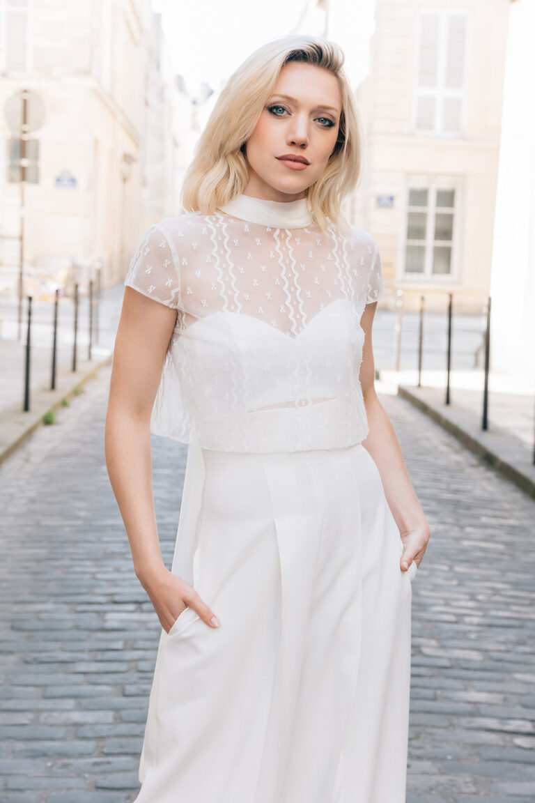 Femme portant une tenue de mariée blanche avec un pantalon et un top en dentelle de Calais-Caudry.