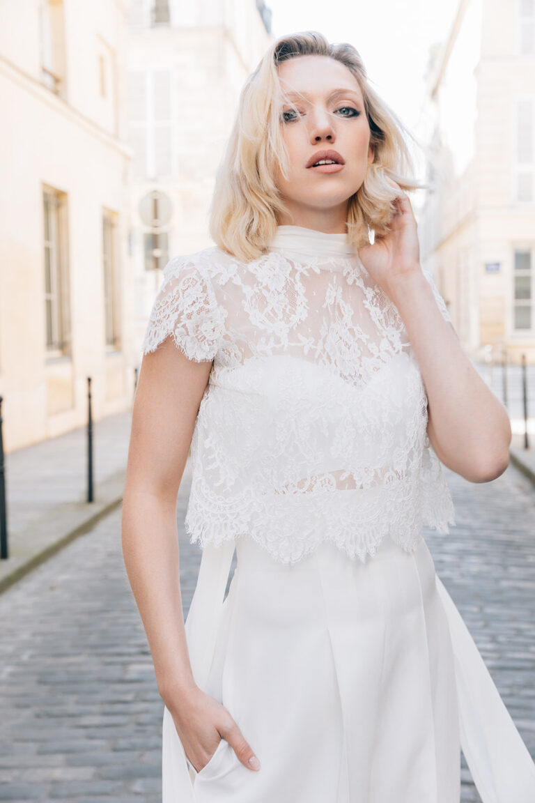 Femme portant une tenue de mariée blanche avec un pantalon et un top en dentelle de Calais-Caudry.