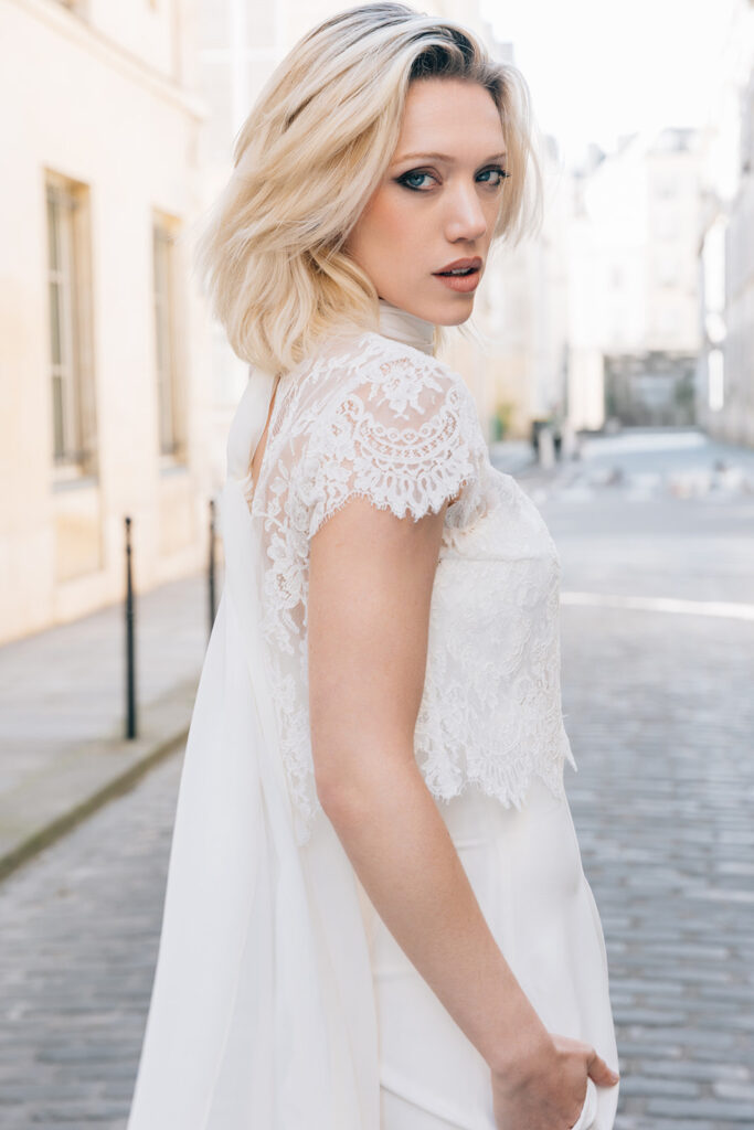 Femme portant une tenue de mariée blanche avec un pantalon et un top en dentelle de Calais-Caudry.
