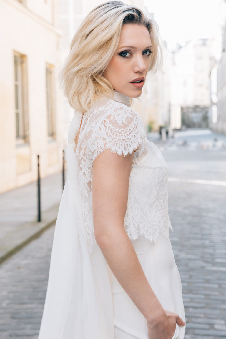 Femme portant une tenue de mariée blanche avec un pantalon et un top en dentelle de Calais-Caudry.