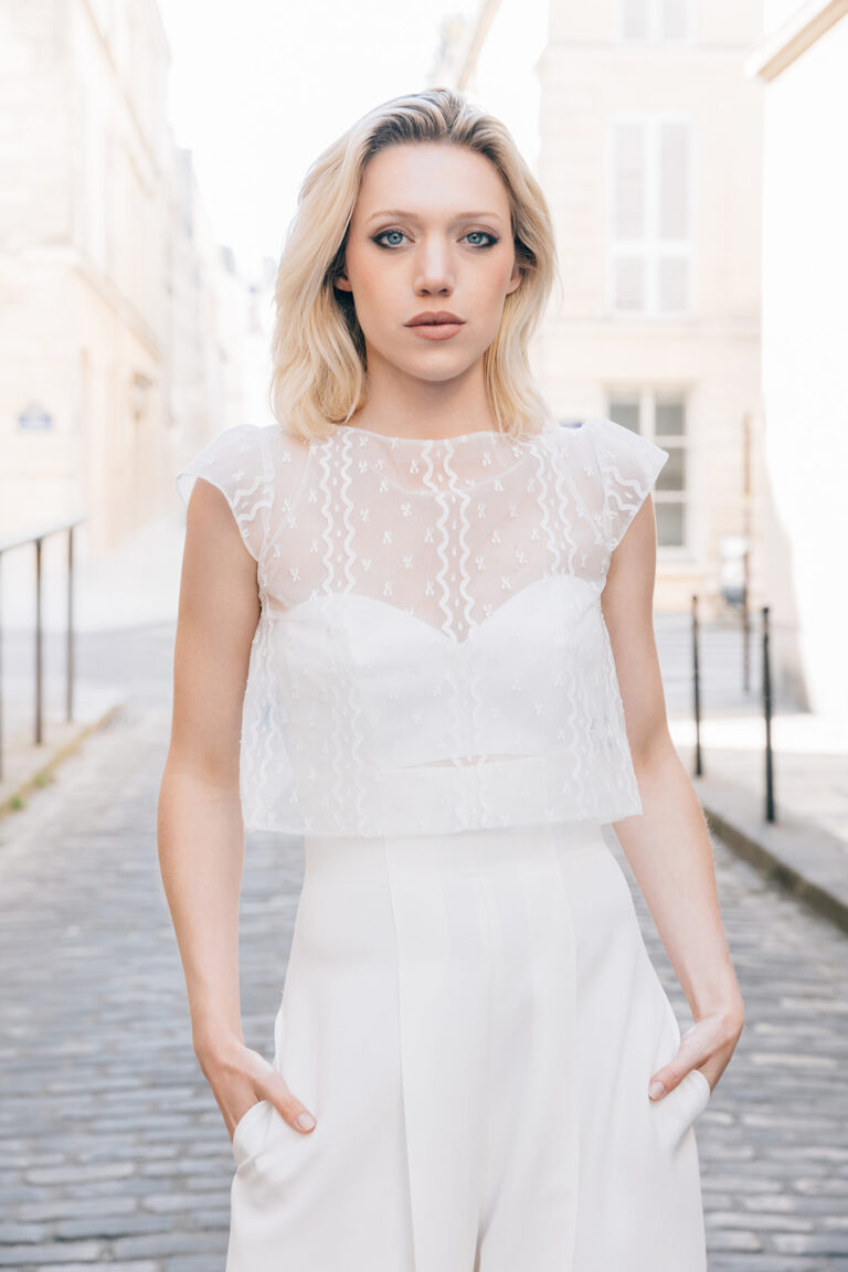 Femme portant une tenue de mariée blanche avec un pantalon et un top en dentelle de Calais-Caudry.