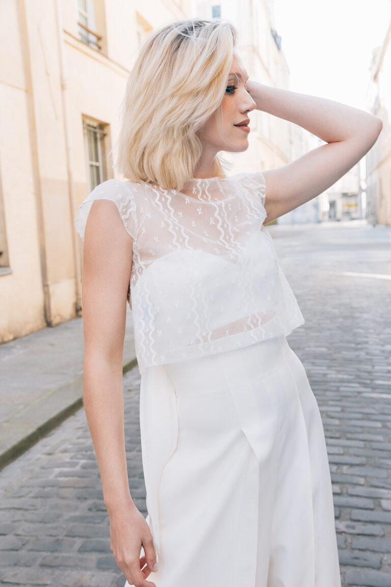 Femme portant une tenue de mariée blanche avec un pantalon et un top en dentelle de Calais-Caudry.