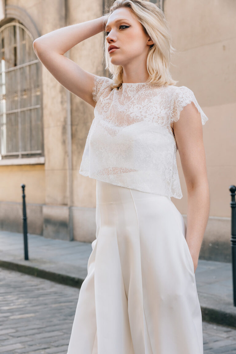Femme portant une tenue de mariée blanche avec un pantalon et un top en dentelle de Calais-Caudry.