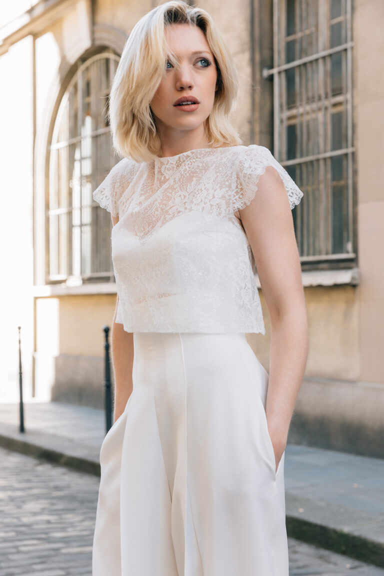 Femme portant une tenue de mariée blanche avec un pantalon et un top en dentelle de Calais-Caudry.