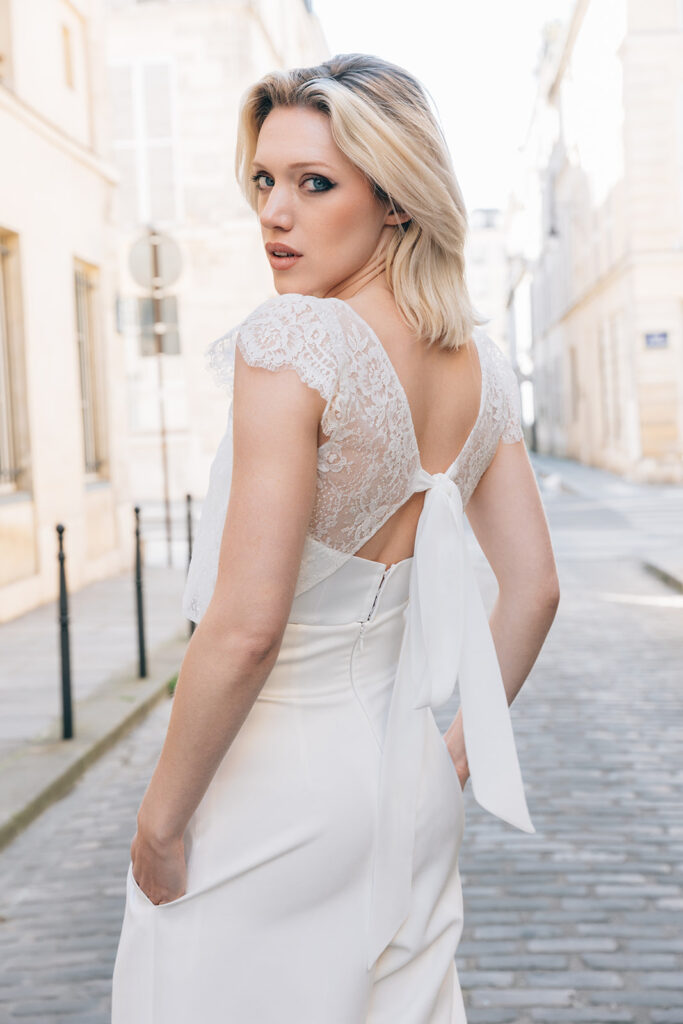 Femme portant une tenue de mariée blanche avec un pantalon et un top en dentelle de Calais-Caudry noué dans le dos.