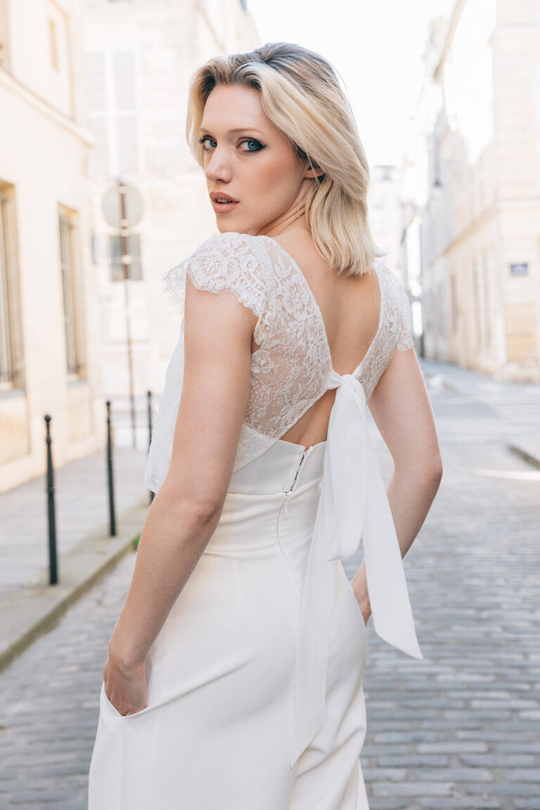 Femme portant une tenue de mariée blanche avec un pantalon et un top en dentelle de Calais-Caudry noué dans le dos.