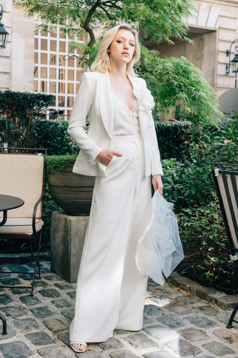 Femme qui porte un ensemble de mariée avec un pantalon, un top et une veste blanche.