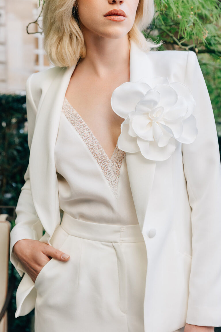 Femme qui porte un ensemble de mariée avec un pantalon, un top et une veste blanche avec une fleur.