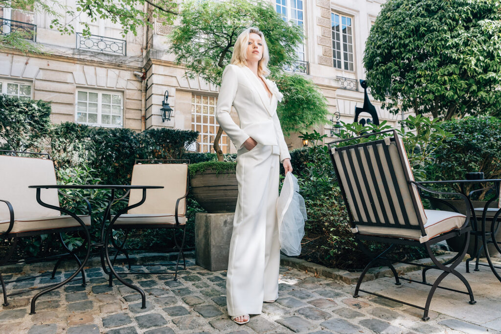 Femme qui porte un ensemble de mariée avec un pantalon, un top et une veste blanche avec une fleur.