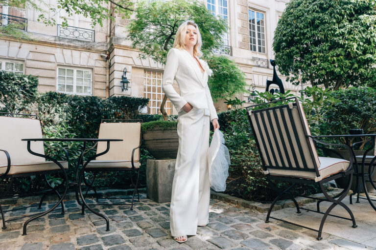 Femme qui porte un ensemble de mariée avec un pantalon, un top et une veste blanche avec une fleur.